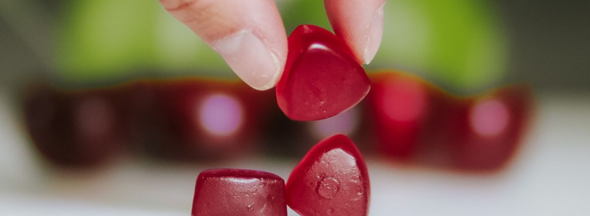 A hand holding a red Cherry Lime CBD gummy.