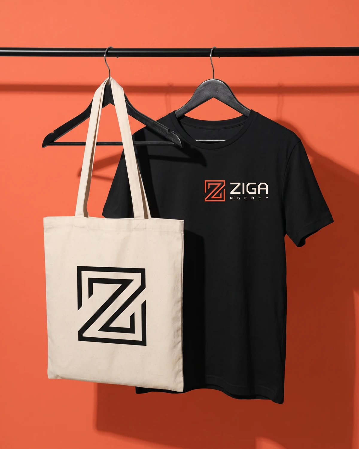 Camiseta preta e ecobag da Ziga penduradas numa arara, contra uma parede coral